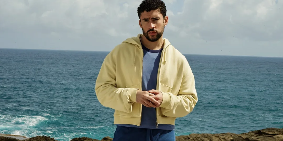 Homme en sweat à capuche beige près de la mer avec ciel nuageux.
