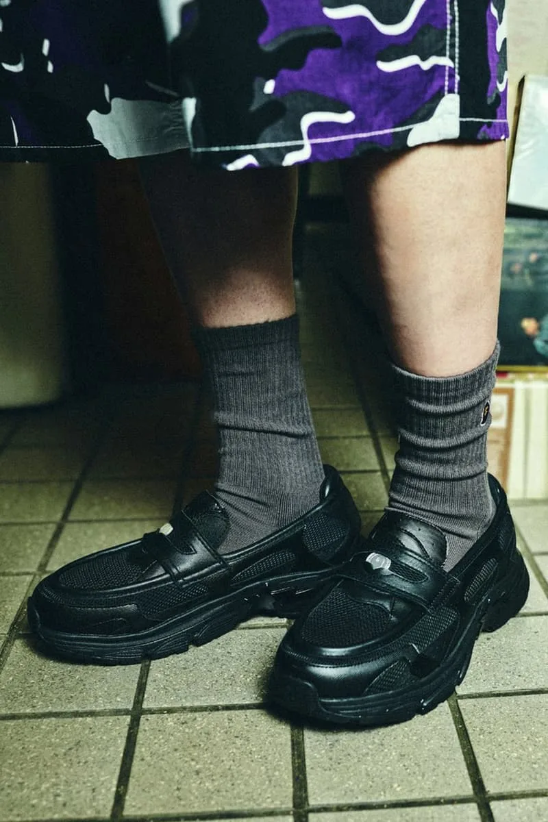 Jambes avec chaussettes grises et mocassins noirs sur un sol carrelé.