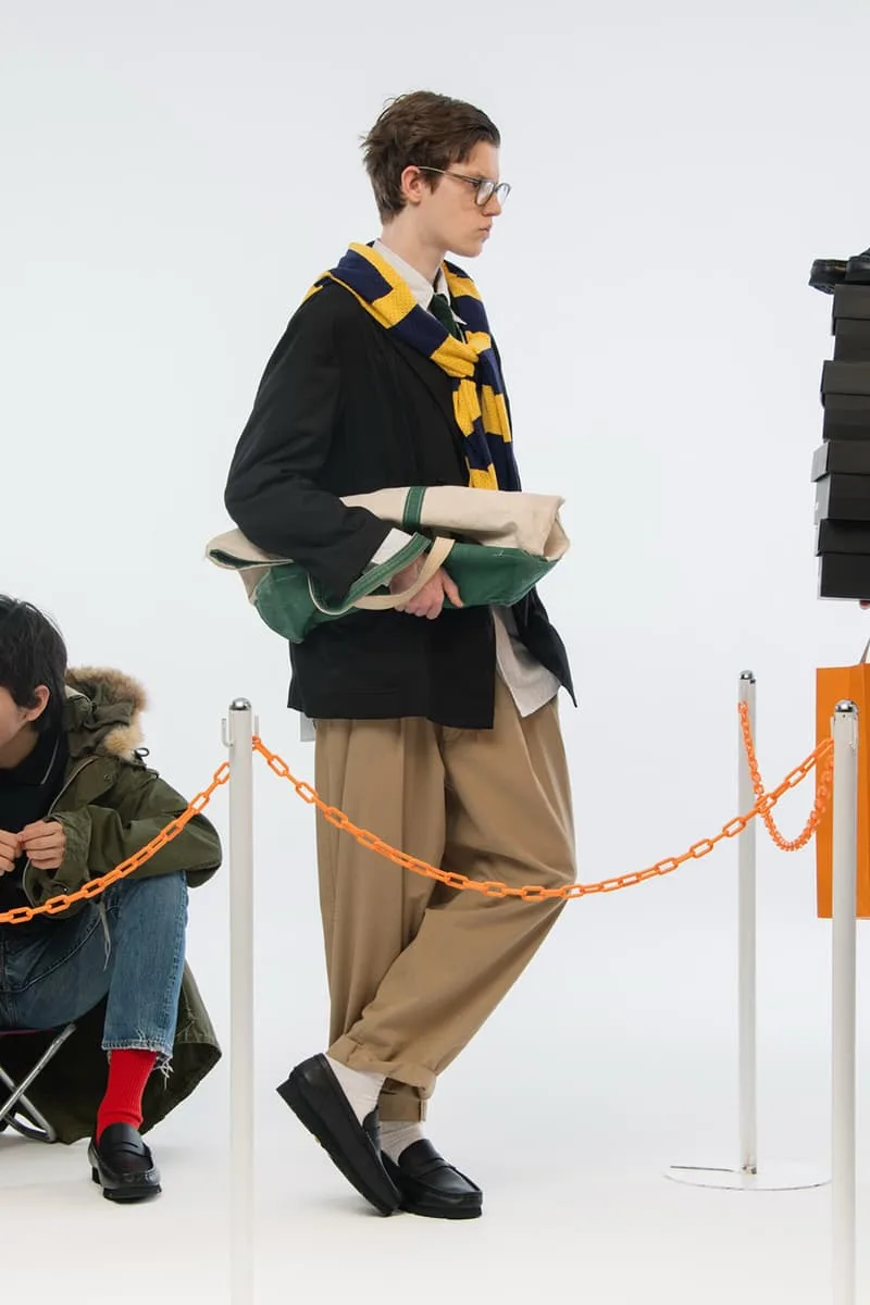 Homme avec écharpe bleue et jaune, veste noire, pantalon beige et lunettes.