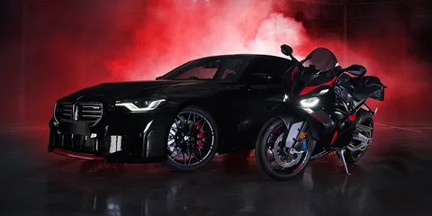 Voiture noire et moto avec fumée rouge en arrière-plan.