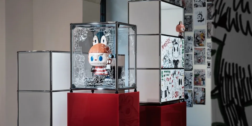 Exposition de jouets avec figurines dans des cubes en verre et art mural en arrière-plan.