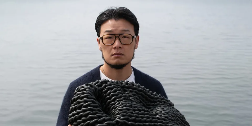 Homme avec des lunettes tenant une corde noire devant l'eau.