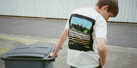 Un garçon portant un T-shirt imprimé à côté d'une poubelle.