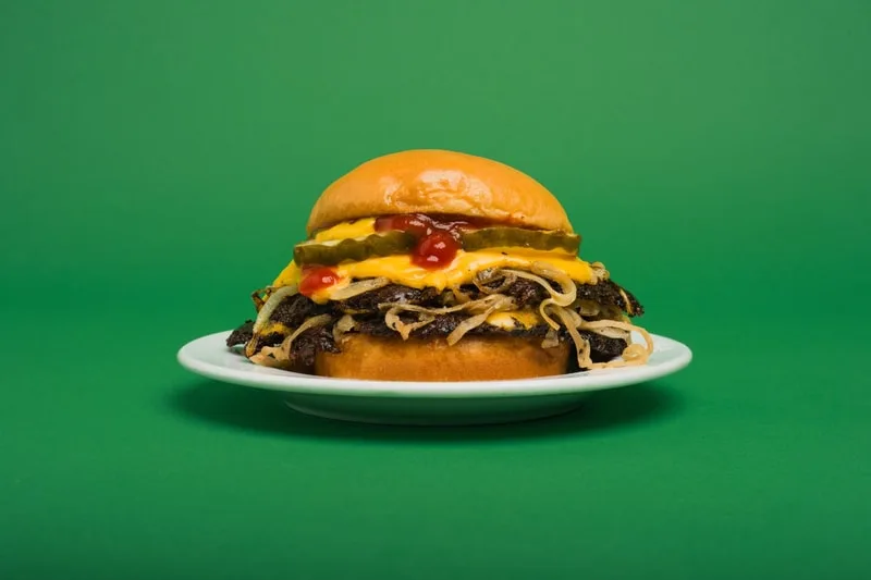Hamburger avec fromage, cornichons et ketchup sur fond vert.