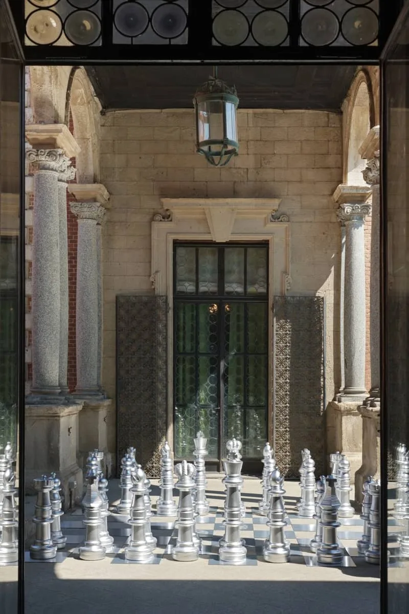 Grand échiquier en plein air avec pièces argentées, entrée de bâtiment historique.