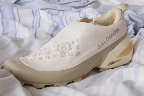 Chaussure Salomon blanche avec un design unique, posée sur un lit à rayures.