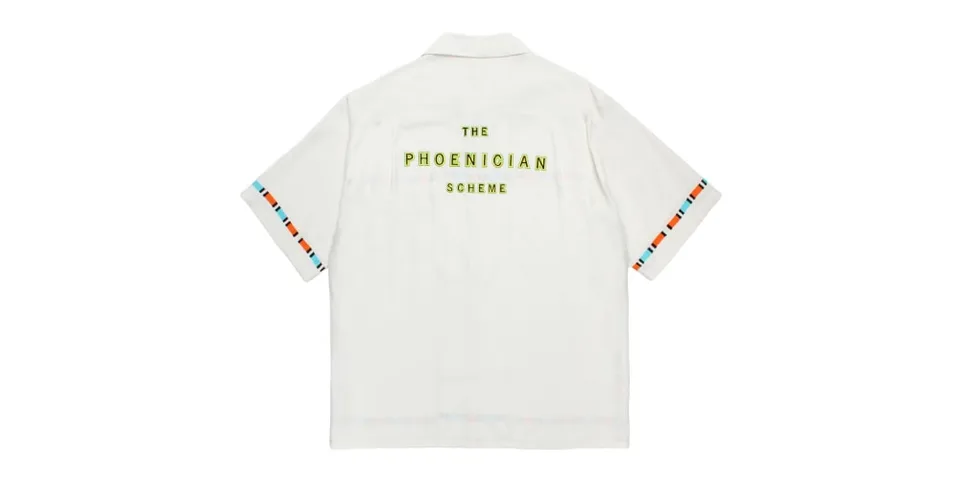 Chemise blanche avec texte jaune "The Phoenician Scheme".