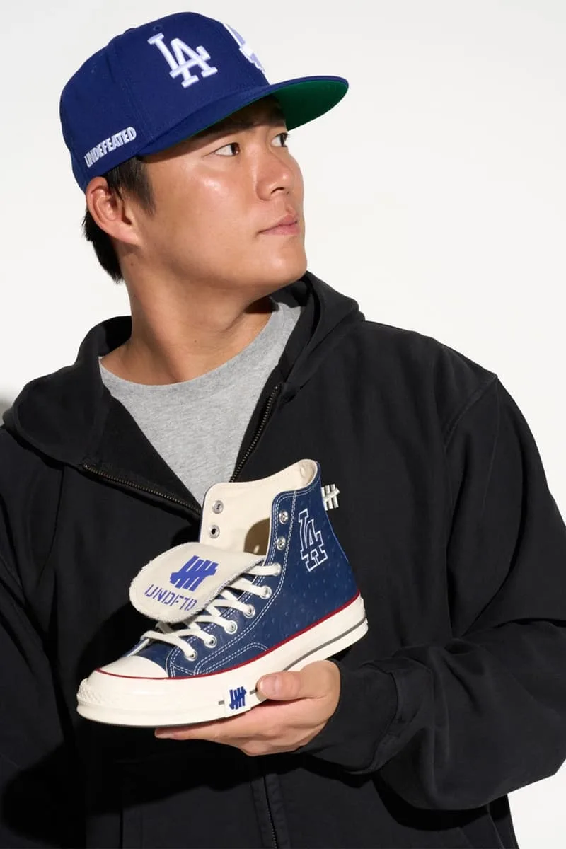 Homme avec casquette bleue tenant une chaussure bleue, logo LA visible.