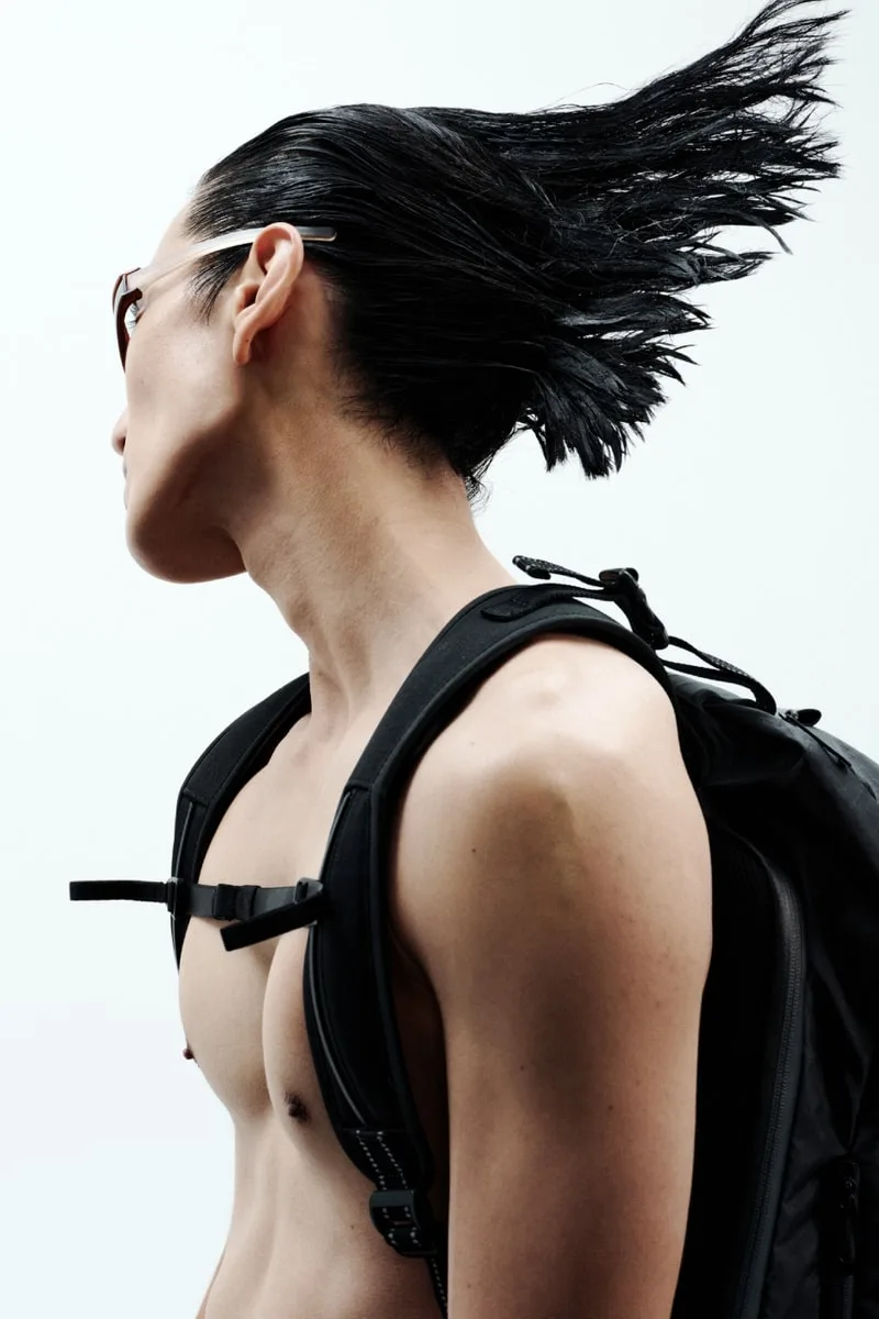Personne aux cheveux en arrière avec un sac à dos sombre, torse nu.