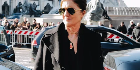 Femme en manteau noir avec lunettes de soleil lors d'un événement en extérieur.