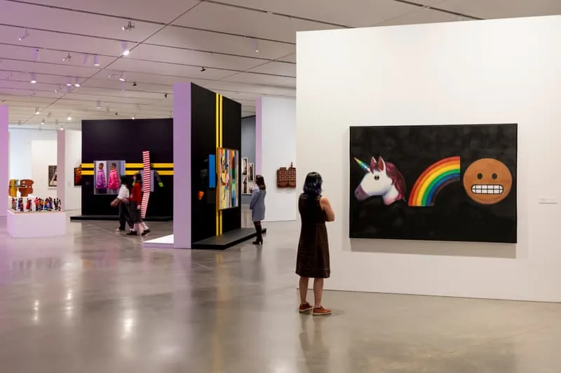 Exposition d'art moderne avec des œuvres colorées sur murs blancs et noirs.