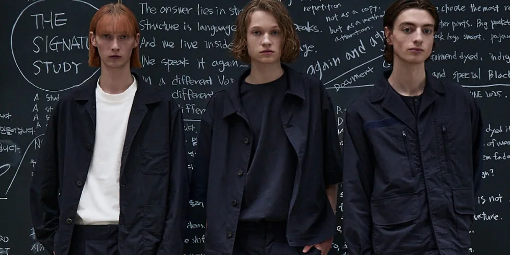 Trois mannequins posant devant un tableau noir avec des écritures blanches.