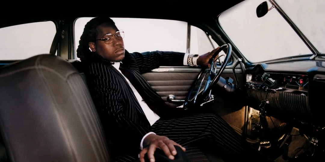 Homme en costume rayé assis dans une voiture vintage.