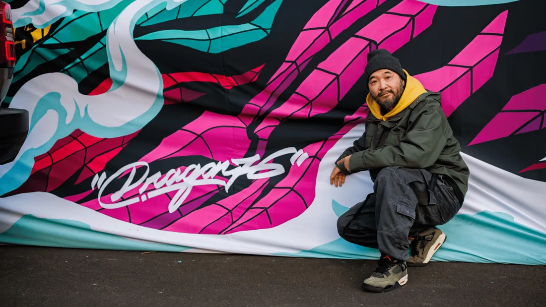 Homme agenouillé devant un graffiti coloré.