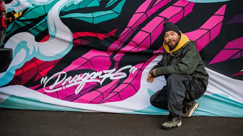 Homme agenouillé devant un graffiti coloré.