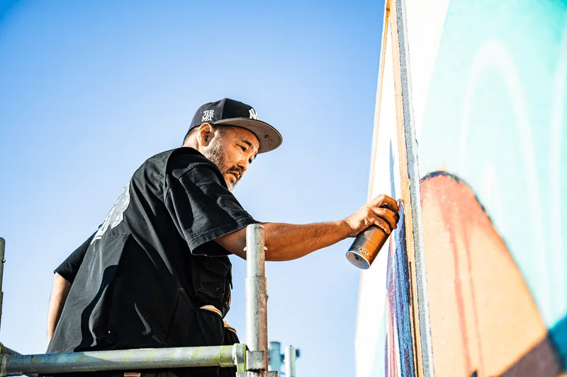 Un homme peignant une fresque murale sur une échelle avec un spray.