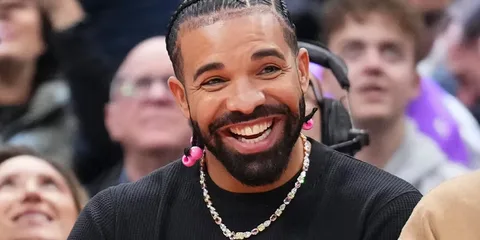 Une personne souriante avec des tresses et un collier, fond flou.