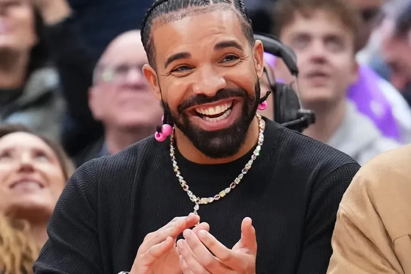 Homme souriant avec collier et boucles d'oreilles roses, foule en arrière-plan