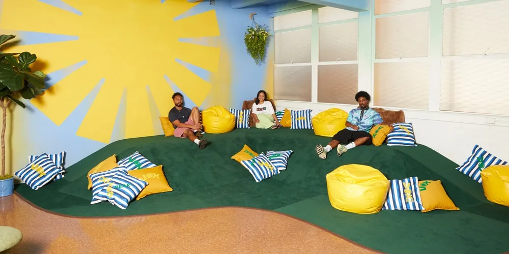 Trois personnes assises sur une colline avec des coussins colorés, intérieur lumineux.
