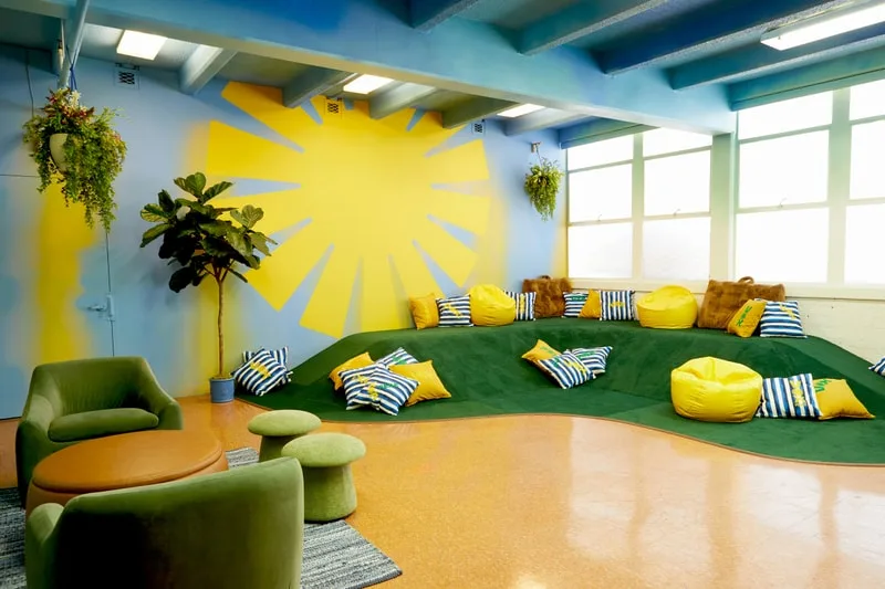 Salle lumineuse avec coussins, plantes et décor ensoleillé.