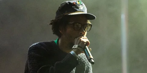 Un homme chante sur scène avec un micro, portant chapeau et lunettes.
