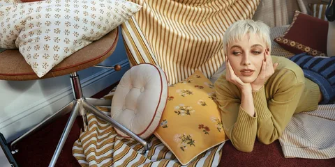 Personne allongée sur un tapis avec oreillers et tissu rayé autour.