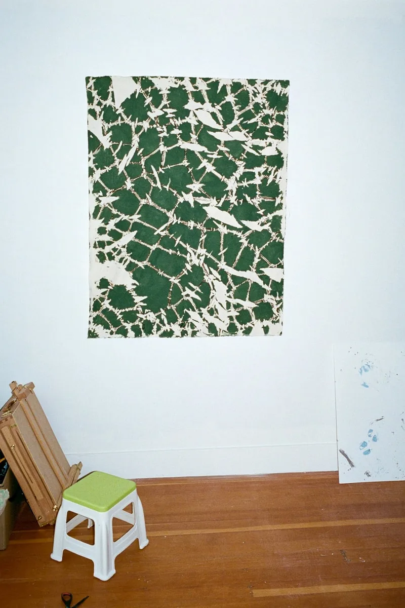 Tissu tie-dye vert accroché au mur, tabouret et toile au sol