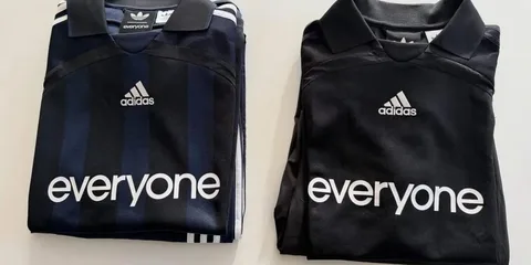 Deux maillots Adidas pliés, bleu marine et noir, avec texte 'everyone'.