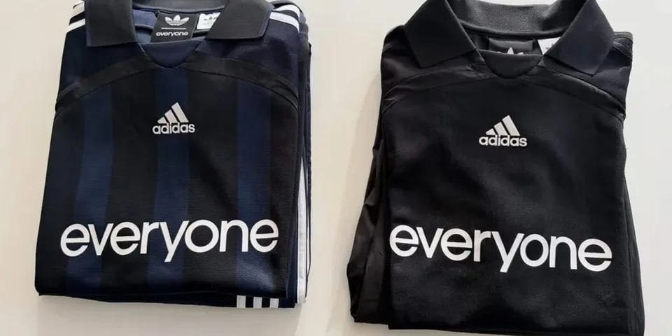 Deux maillots Adidas pliés, bleu marine et noir, avec texte 'everyone'.