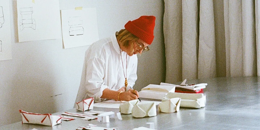 Personne avec bonnet rouge travaillant à une table, entourée de croquis et prototypes.