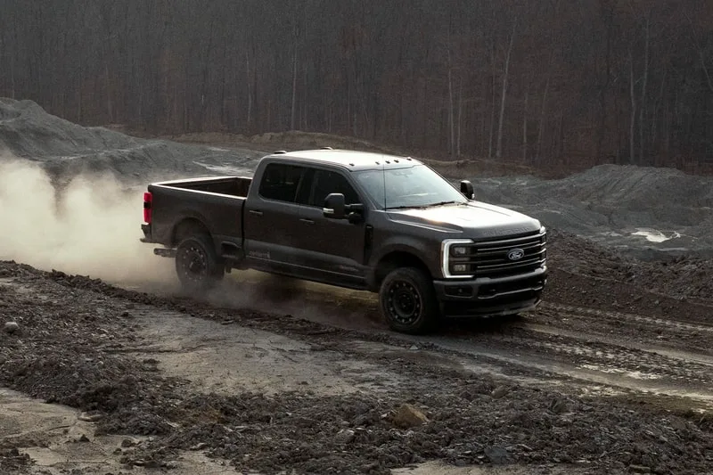 Camionnette noire conduisant sur un terrain boueux avec une forêt en arrière-plan.