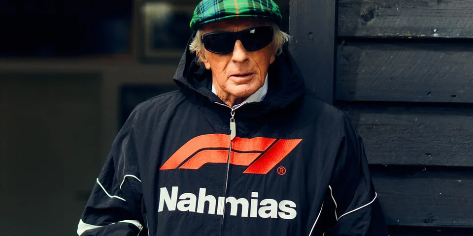 Homme avec manteau Nahmias et casquette verte, lunettes de soleil noires.