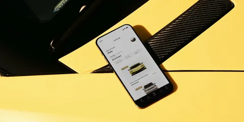 Smartphone sur une voiture jaune montrant une application de location de voitures.
