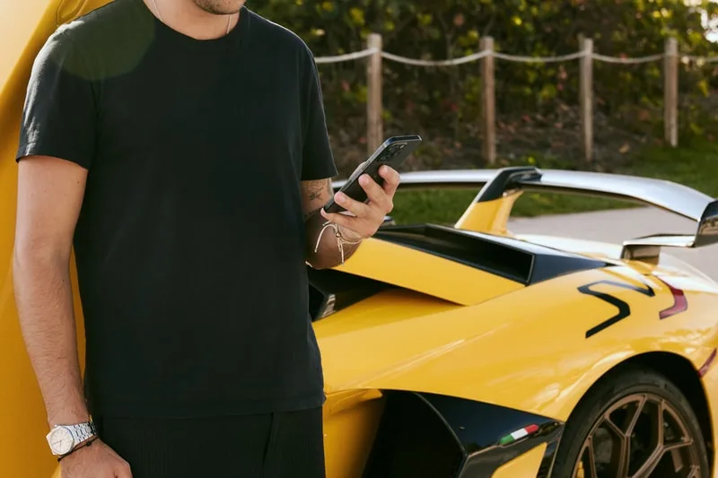 Homme en noir utilisant un téléphone devant une voiture jaune sportive.