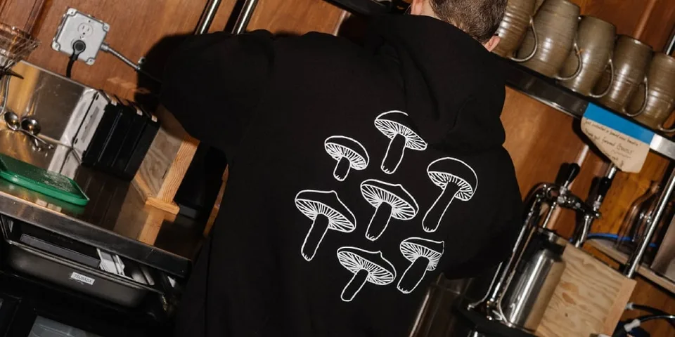Personne portant un sweat noir avec des champignons blancs, dos à la caméra.