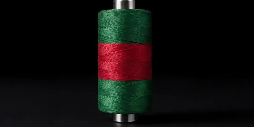Bobine de fil vert et rouge sur fond noir.
