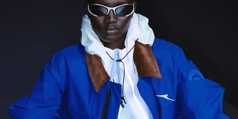 Personne portant des lunettes et une veste bleue sur fond sombre.