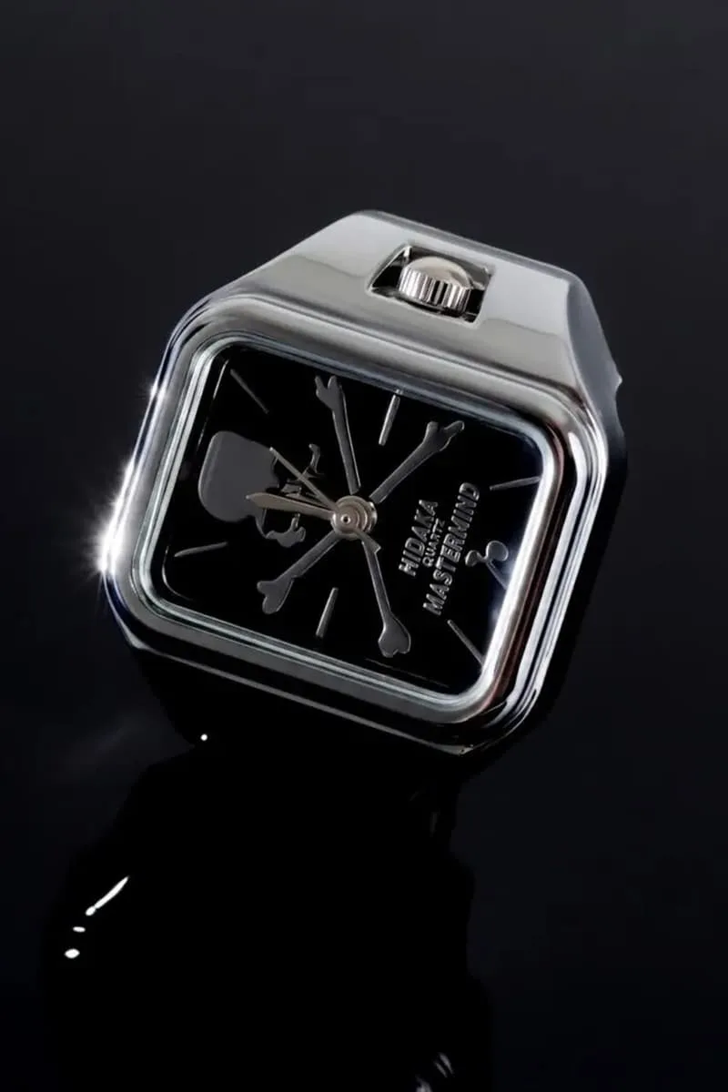 Montre carrée avec crâne et os croisés sur fond noir.