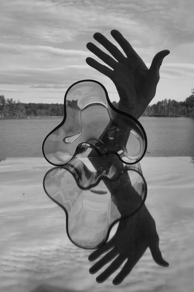 Ombre de mains et sculpture en verre avec reflet sur fond de lac