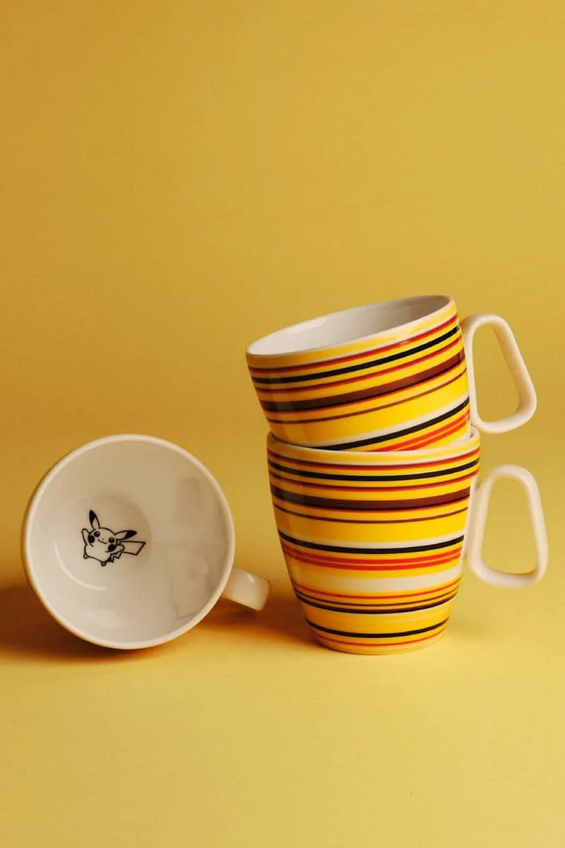 Tasses à rayures colorées sur fond jaune, intérieur illustré d'un personnage.