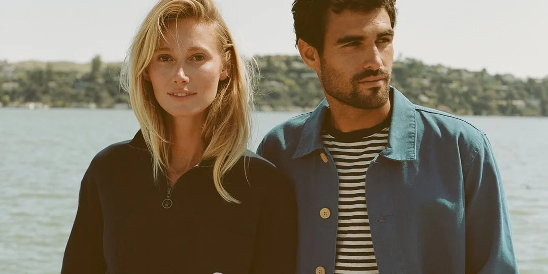 Un couple pose devant un lac, habillé de vêtements décontractés.