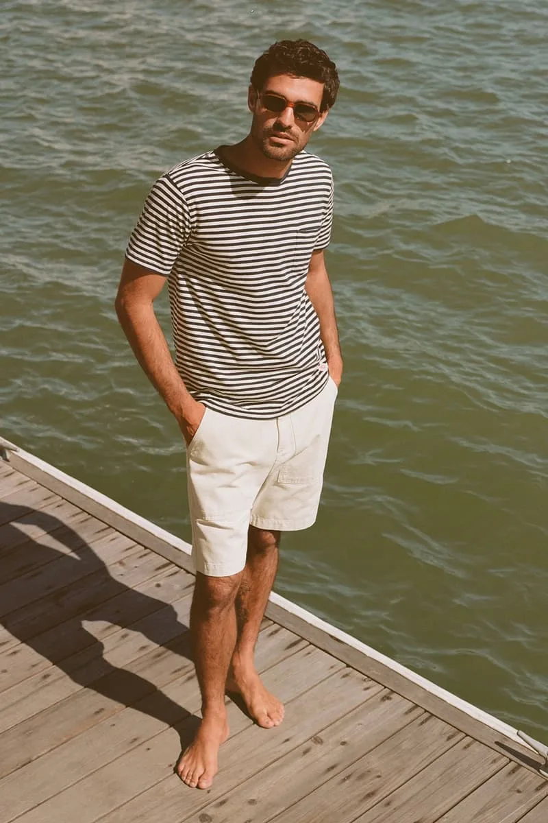 Homme en t-shirt rayé et short blanc sur un quai au bord de l'eau.