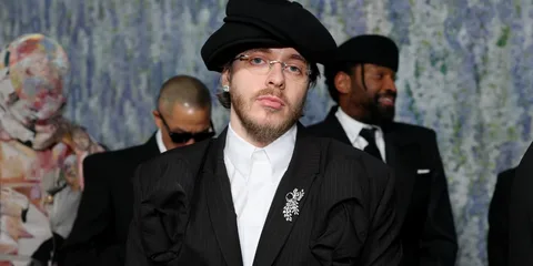 Homme avec béret noir et lunettes, portant un costume élégant.