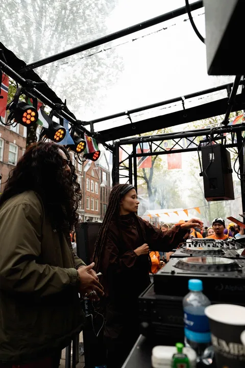 DJ en plein air avec un public, sous des lumières et des drapeaux.