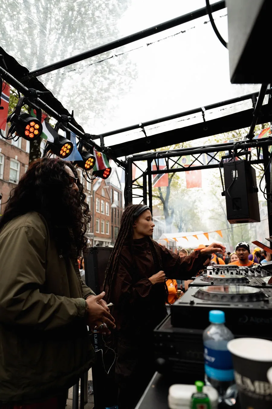 DJ en plein air avec un public, sous des lumières et des drapeaux.