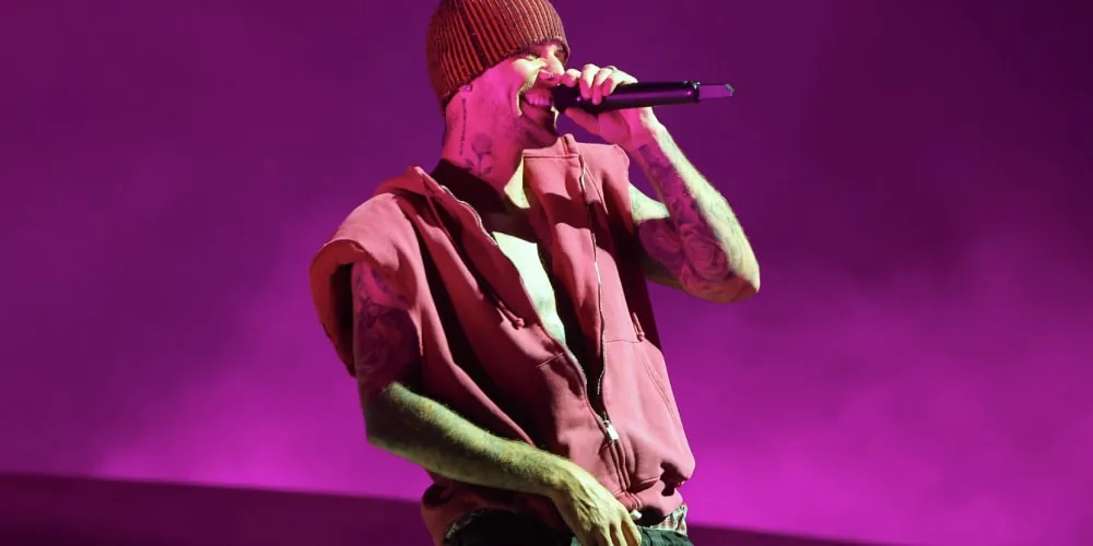 Chanteur avec beanie et microphone sur scène, fond violet.