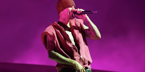 Chanteur avec beanie et microphone sur scène, fond violet.