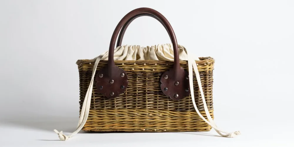 Panier en osier avec poignées en cuir et doublure en tissu blanc.