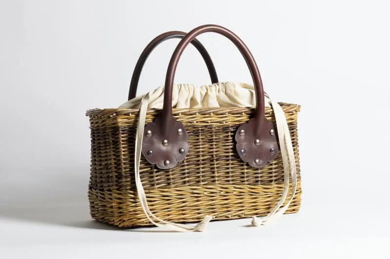 Panier en osier avec poignées en cuir marron et doublure en tissu beige.