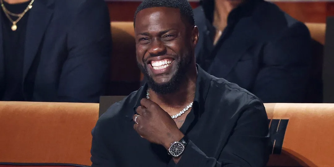 Homme souriant en chemise noire assis dans un théâtre.